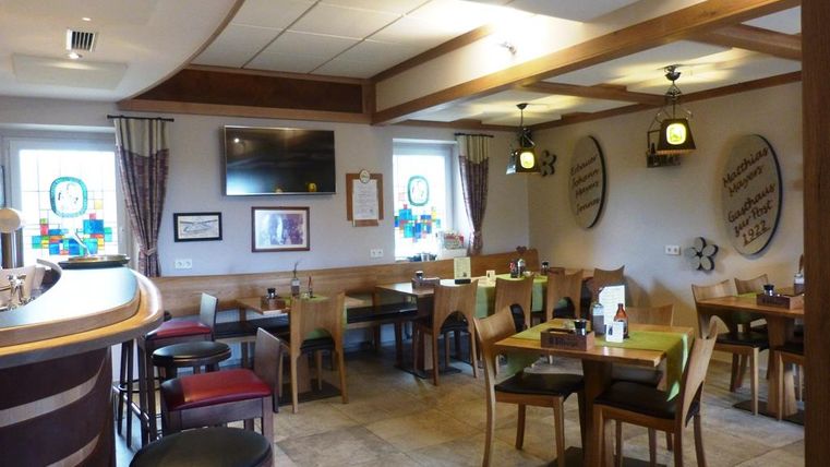 An inviting restaurant with wooden furniture and warm lighting. There are tables with chairs and a bar in a cozy atmosphere.