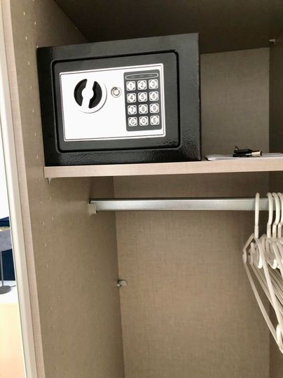 A black security cabinet with a digital combination lock, in an open cabinet. Hangers are also visible in the cabinet.