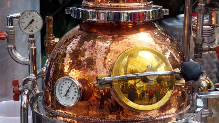 Een koperen distilleerderij met een glanzend oppervlak en verschillende drukmeters. Het is een onderdeel van een distillatieproces voor de productie van sterke dranken.