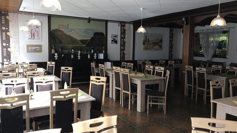 Een gezellig restaurant met lichte tafels en stoelen. De muren zijn versierd met afbeeldingen, en er heerst een ontspannen sfeer.