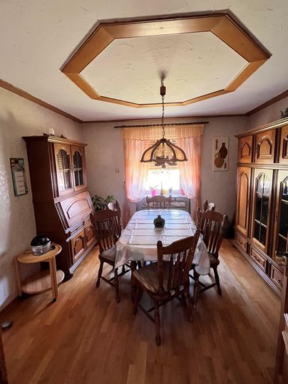 Ein gemütlicher Essbereich mit einem großen Holztisch und mehreren Stühlen. Ein Fenster mit Vorhängen sorgt für natürliches Licht und eine warme Atmosphäre.