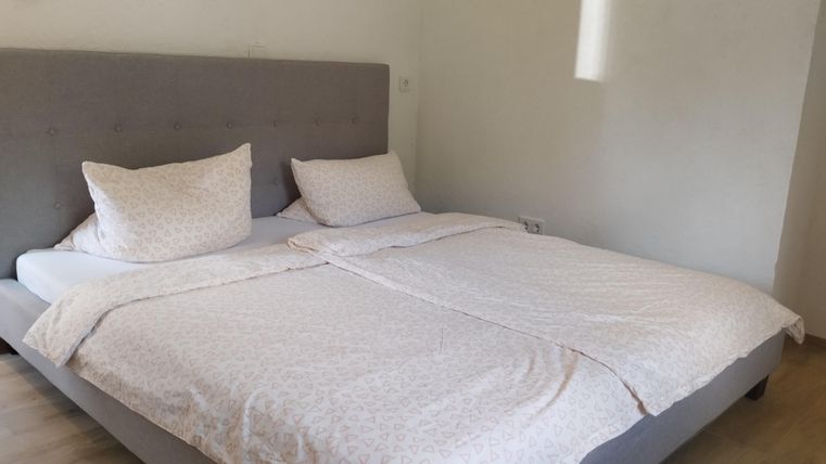 Een gezellige slaapkamer met een groot bed en lichte beddengoed. De muren zijn in neutrale kleuren en er is veel natuurlijk licht.