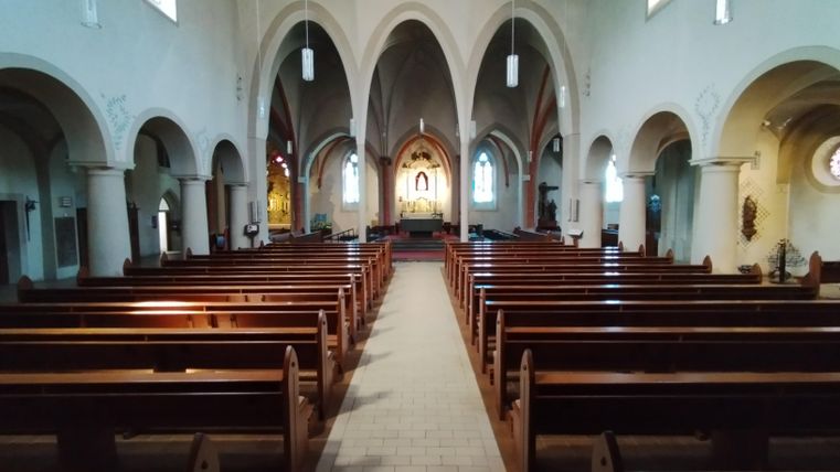 Eine ruhige Kirche mit Holzbankreihen und hohen, gewölbten Decken. Im Hintergrund ist ein Altar zu sehen.