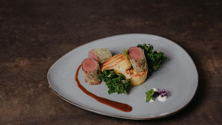 Un plat élégant avec de la viande tendre, entouré de légumes et d'une sauce décorative. Le repas est joliment présenté sur une assiette moderne.