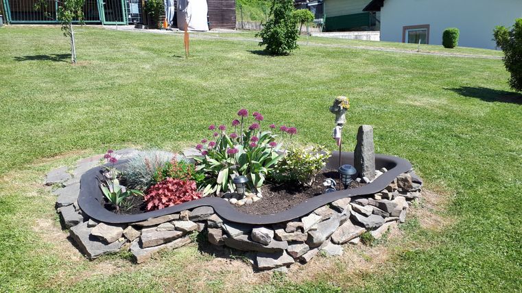 A beautiful garden with colorful flowers and a decorative rock garden. The layout has a curved shape and is surrounded by green grass.