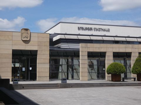 Eine moderne Stadtverwaltung mit einer klaren Fassade und großen Fenstern. Vor dem Gebäude befinden sich gepflegte Pflanzen.
