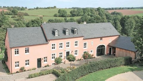 Ein schönes, rosa Haus mit einem großen Garten und sichtbaren Bäumen in der Umgebung. Die Landschaft ist grün und hügelig.
