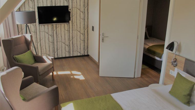 Ein modernes Hotelzimmer mit zwei bequemen Stühlen und einem Fernseher an der Wand. Die Räume sind hell und freundlich eingerichtet, mit grünen Akzenten.