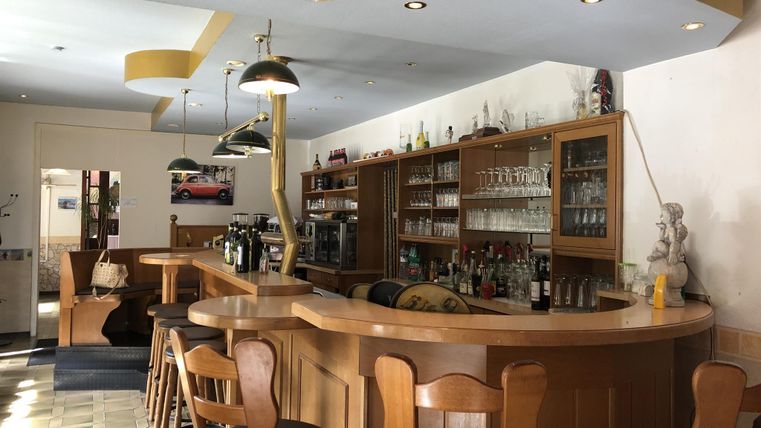 Een uitnodigende bar met houten toog en een assortiment aan dranken. De ruimte is helder en modern ingericht.