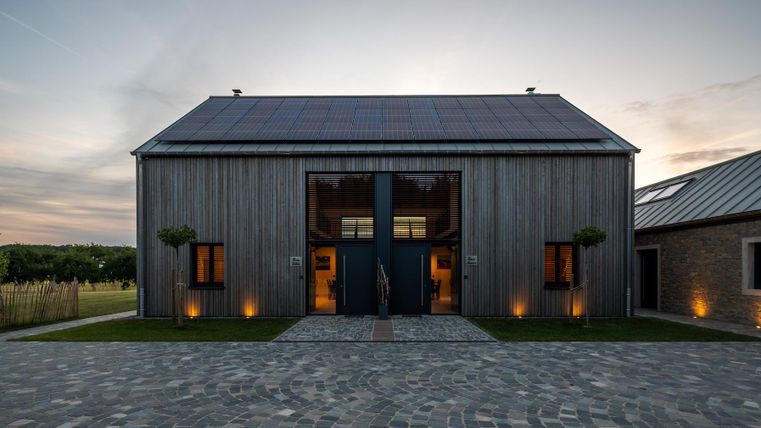 Ein modernes Gebäude mit Holzfassade und großen Glasfronten. Die Umgebung ist gepflegt und der Himmel zeigt den Übergang zum Abend.
