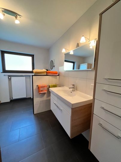 Ein modernes Badezimmer mit einem hellen Waschbecken und weißen Wänden. Handtücher in verschiedenen Farben liegen ordentlich bereit.