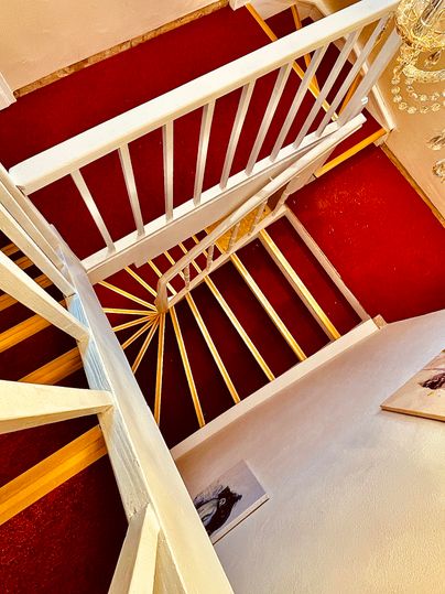 Un escalier en colimaçon moderne avec une balustrade blanche et un tapis rouge. À l'arrière-plan, des murs de teinte claire sont visibles.