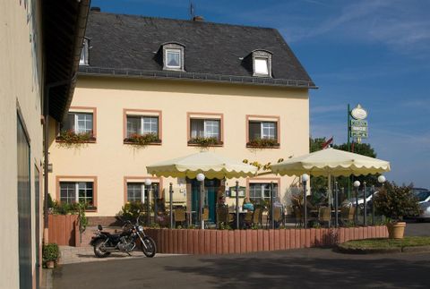 Ein gemütliches Gasthaus mit blühenden Fenstern und einem Terrassenbereich. Draußen steht ein Motorrad und es gibt Sonnenschirme zum Entspannen.