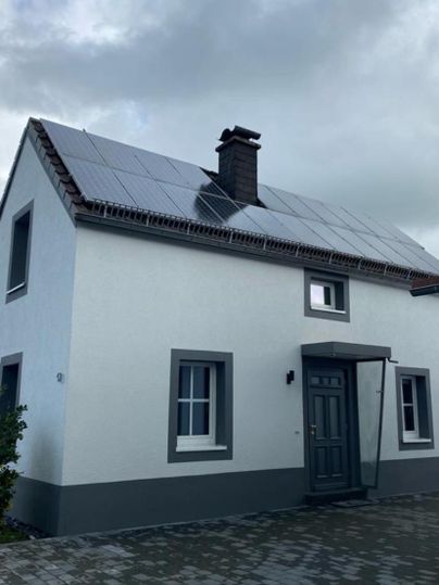 Ein modernes Haus mit Solarzellen auf dem Dach. Der Himmel ist bewölkt und die Umgebung ist ruhig.