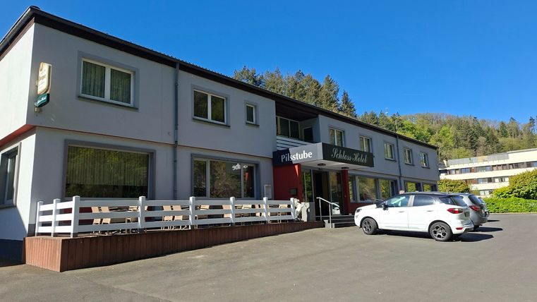 Ein kleines Gasthaus mit einer hellen Fassade und einem einladenden Eingangsbereich. Vor dem Gebäude stehen mehrere Autos parken.