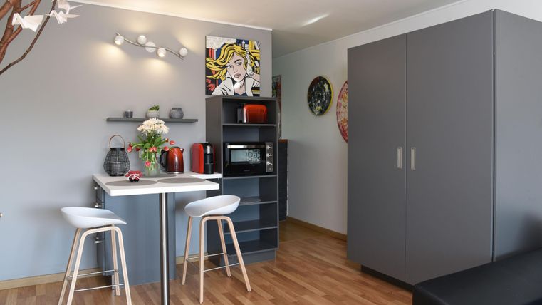 Une cuisine moderne avec une petite table et deux chaises. En arrière-plan, il y a un mur de placard gris et des éléments décoratifs sur les murs.