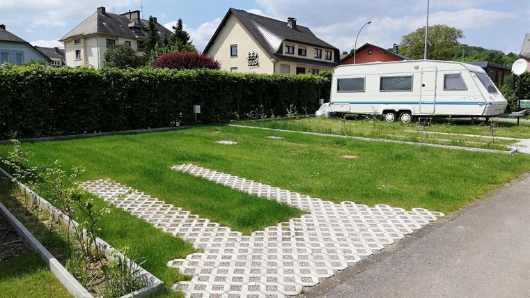Een groene recreatielocatie met een stacaravan. Op de achtergrond zijn enkele huizen en een sportveld te zien.