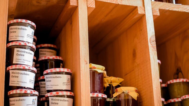 Planken met verschillende marmelades en gelei. De glazen hebben rood-witte geblokte deksels en gelabelde etiketten.