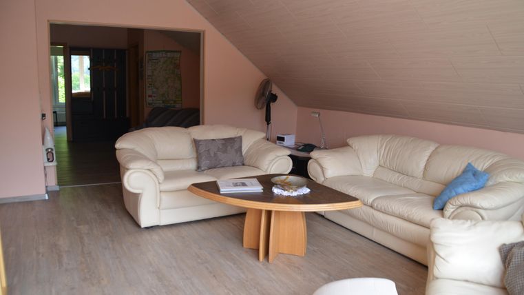 Cozy living room with white leather sofas and a round table. The walls are painted in a soft pink hue, and the room has a bright, inviting atmosphere.