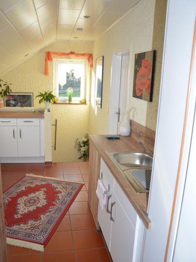 A cozy kitchen corner with a small sink and a rug. Bright walls and plants create a friendly atmosphere.