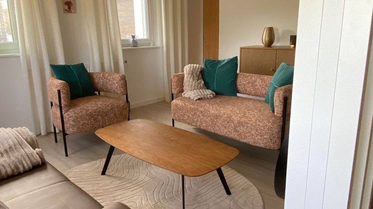 Ein modernes Wohnzimmer mit zwei stilvollen Sesseln und einem Sofa. Der Tisch aus Holz steht auf einem runden Teppich und die Wände sind hell gestrichen.
