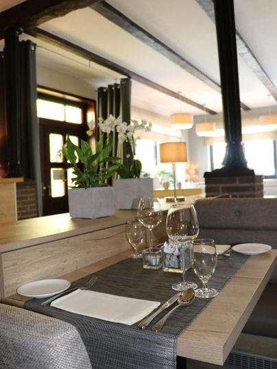 Une table de restaurant élégante avec une belle nappe et de la vaisselle. À l'arrière-plan, des plantes décoratives et un éclairage doux sont visibles.