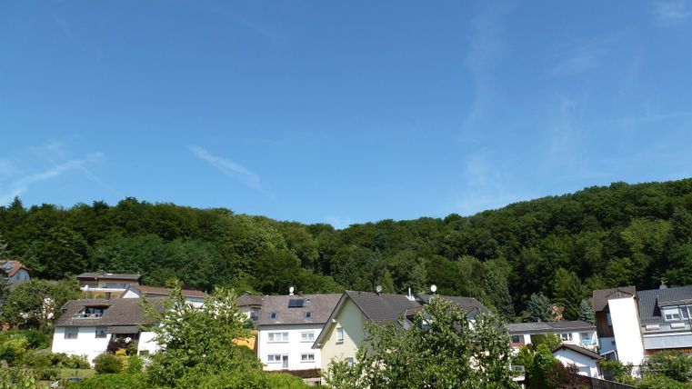 Eine idyllische Wohngegend mit modernen Häusern und üppigem Grün. Der Himmel ist klar und bleu, umgeben von sanften Hügeln.