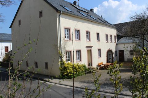 Een charmant huis met lichte stucco en raamkozijnen in pasteltinten. Op de voorgrond staan planten en een rustige straat.