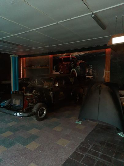 Eine alte Garage mit zwei dekorativen Autos. Eines der Autos steht im Vordergrund, während das zweite an der Wand hängt.