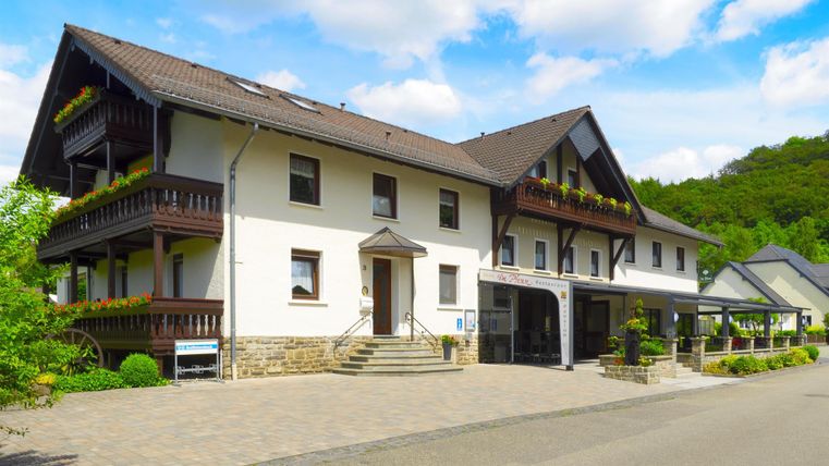 Ein gemütliches Hotelgebäude mit mehreren Stockwerken und Balkonen. Umgeben von grünen Bäumen und einem klaren Himmel.