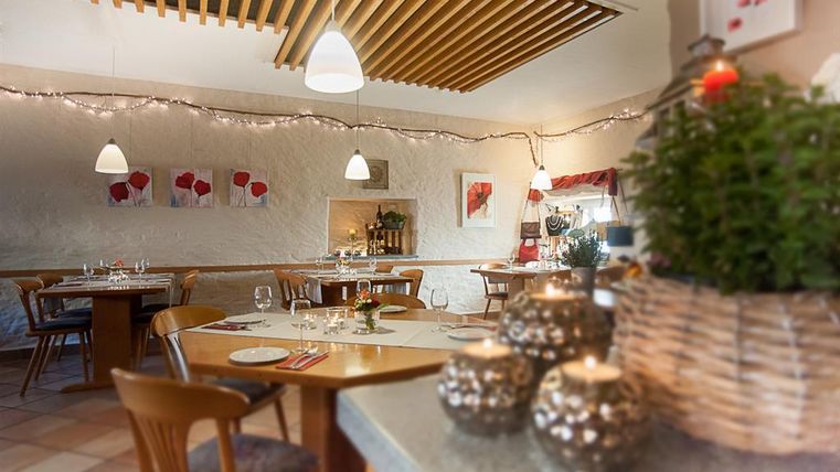 Ein gemütliches Restaurant mit wooden Decke und stimmungsvollem Licht. Die Tische sind liebevoll gedeckt und dekoriert mit Pflanzen und Kerzen.