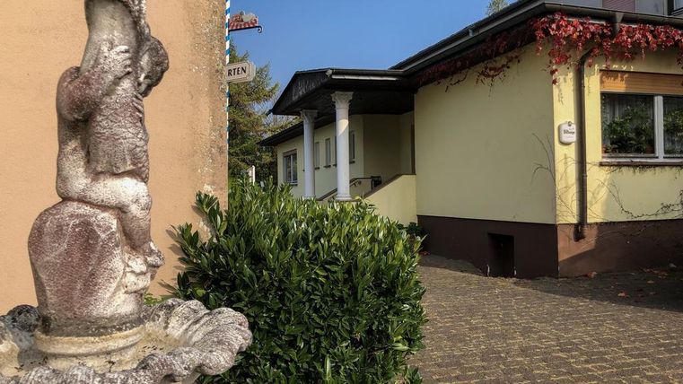 Une statue décorative se dresse devant un bâtiment à la façade jaune et aux buissons verts. Le chemin mène à une entrée de maison au look amical.