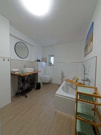 Salle de bain moderne avec une baignoire autoportante et une étagère en bois.
Des murs clairs et un grand miroir créent une atmosphère accueillante.