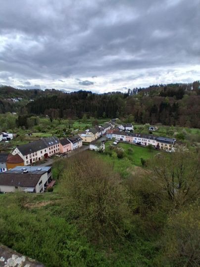Un paysage tranquille avec un petit village, entouré de champs verts et d'arbres. Le ciel est nuageux, créant une atmosphère d'ambiance.