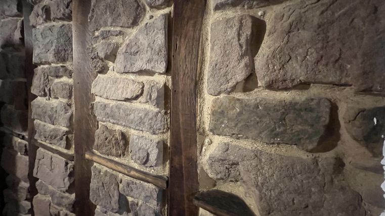 Een muur van natuurstenen met een houten frame. De stenen zijn onregelmatig en in verschillende maten.