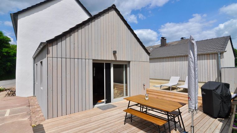 Ein modernes Haus mit Holzverkleidung und einer Terrasse. Auf der Terrasse befindet sich ein Tisch und ein Grill, ideal für entspannte Tage im Freien.