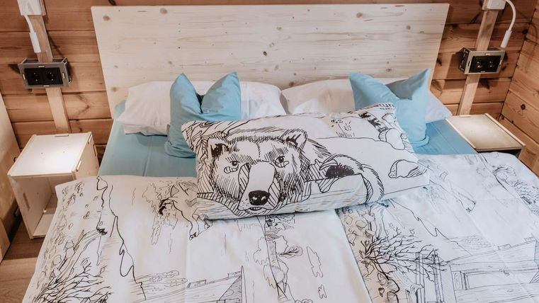 Ein gemütliches Schlafzimmer mit einem Holzrahmenbett. Die Bettwäsche hat ein kreatives Design mit einem Bärenmotiv und es gibt hellblaue Kissen.