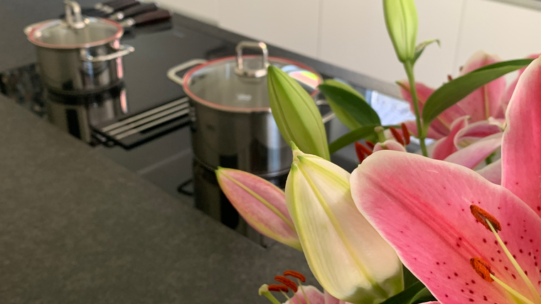Een moderne keuken met een zwart fornuis en twee pannen. Op de voorgrond bloeien roze lelies.