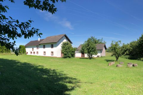 A quiet country house in the middle of a green meadow. The sky is blue and clear, surrounded by a few trees.