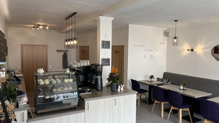 A modern café with a counter that offers coffee and snacks. The space is bright and inviting, with tables and chairs arranged in a cozy manner.