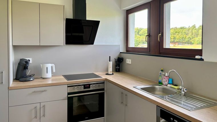 Eine moderne Küche mit Holzarbeitsplatte und Edelstahlgeräten. Neben dem Fenster ist eine gemütliche Aussicht auf die Natur.