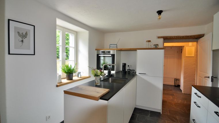 Eine moderne Küche mit weißen Möbeln und eleganter Arbeitsplatte. Sie hat große Fenster, die viel Licht hereinlassen.