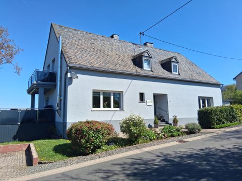 Une maison lumineuse à deux étages avec une façade grise et un toit à pignon. Le jardin est bien entretenu et il y a un chemin devant la maison.
