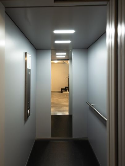 Ein moderner Aufzug mit hellen Wänden und einem klaren Blick auf eine Treppe. Die Beleuchtung sorgt für eine freundliche Atmosphäre.