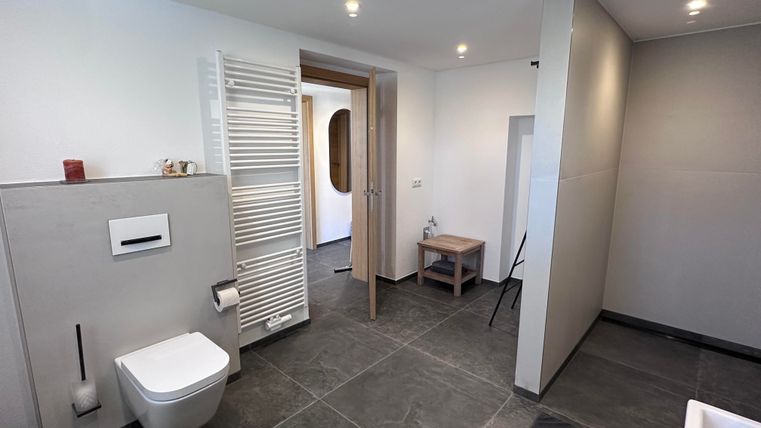 Ein modernes Badezimmer mit schlichten, eleganten Möbeln. Es gibt eine Toilette, einen Heizkörper und eine Badewanne in neutralen Farben.