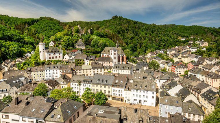 Eine malerische Stadt mit bunten Häusern und grünen Hügeln im Hintergrund. Der Himmel ist klar und blau, was die Schönheit der Landschaft unterstreicht.