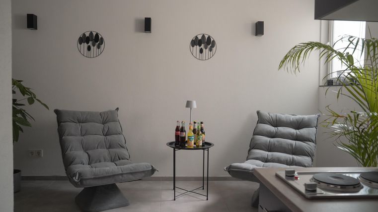 A cozy room with two gray armchairs and a small table. Decorative pictures hang on the wall, and there is a plant in the corner.