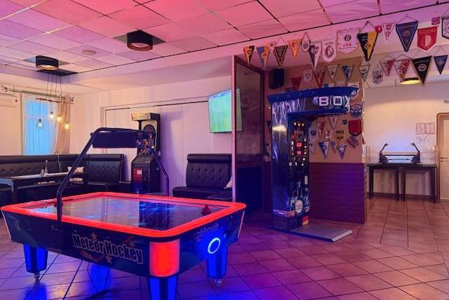 Een entertainmentruimte met een airhockeytafel en gokkasten. Aan de muren hangen verschillende clubvlaggen.