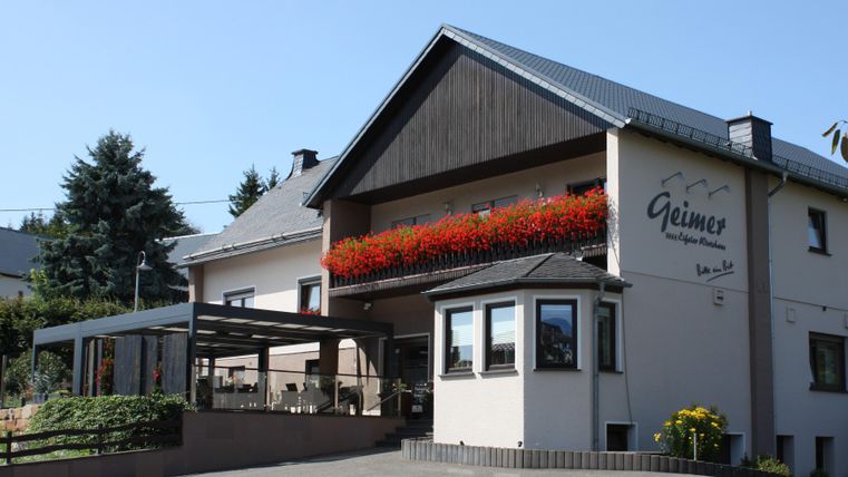 Ein charmantes Haus mit blühenden Balkonpflanzen. Die sonnige Fassade und der einladende Außenbereich schaffen eine freundliche Atmosphäre.