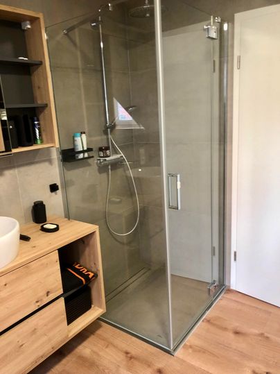 A modern glass shower with an elegant shower fixture. The surrounding area is bright and designed in a minimalist style.